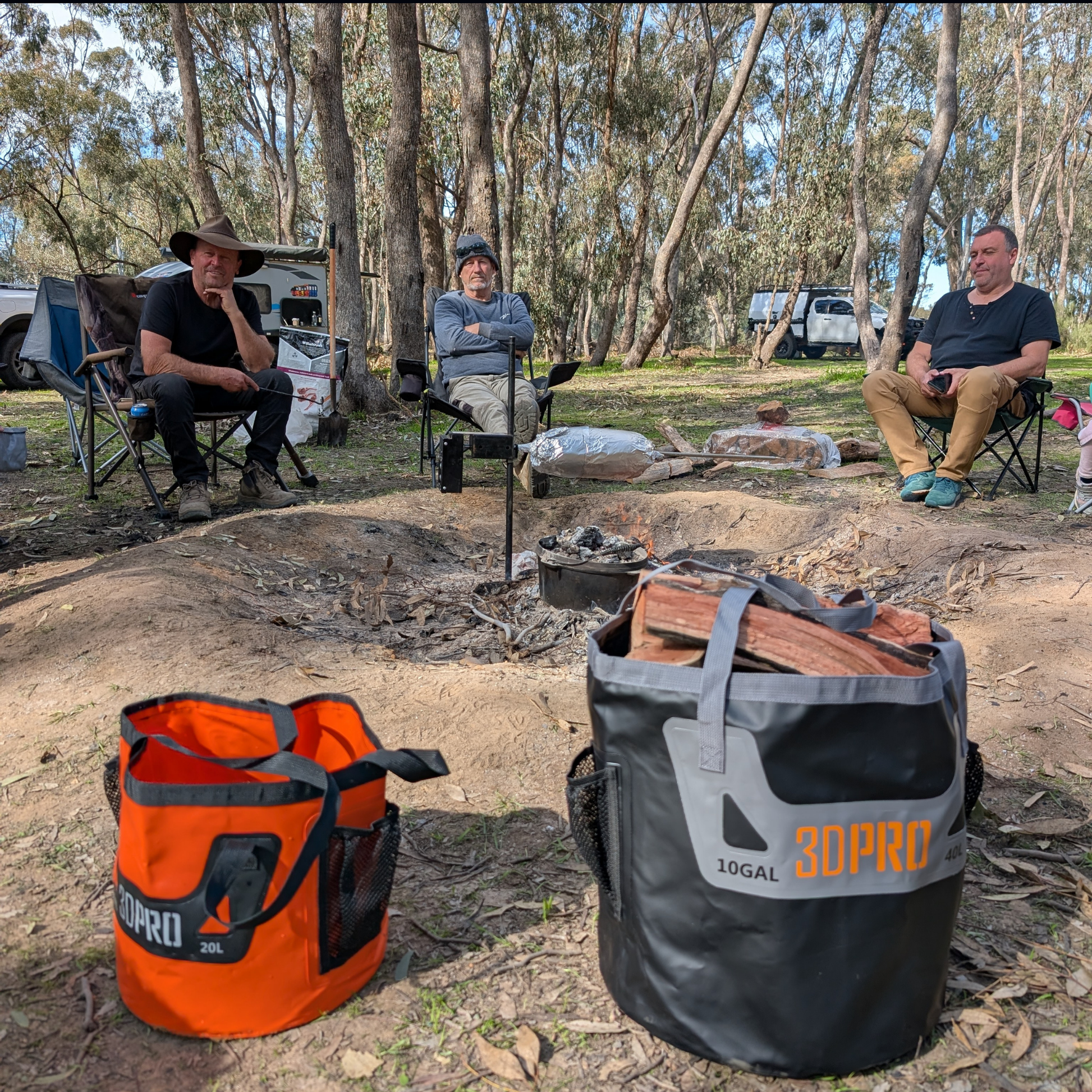 Three people sitting around a campfire with camping gear including orange and black folding buckets '3DPRO' in a forest setting.