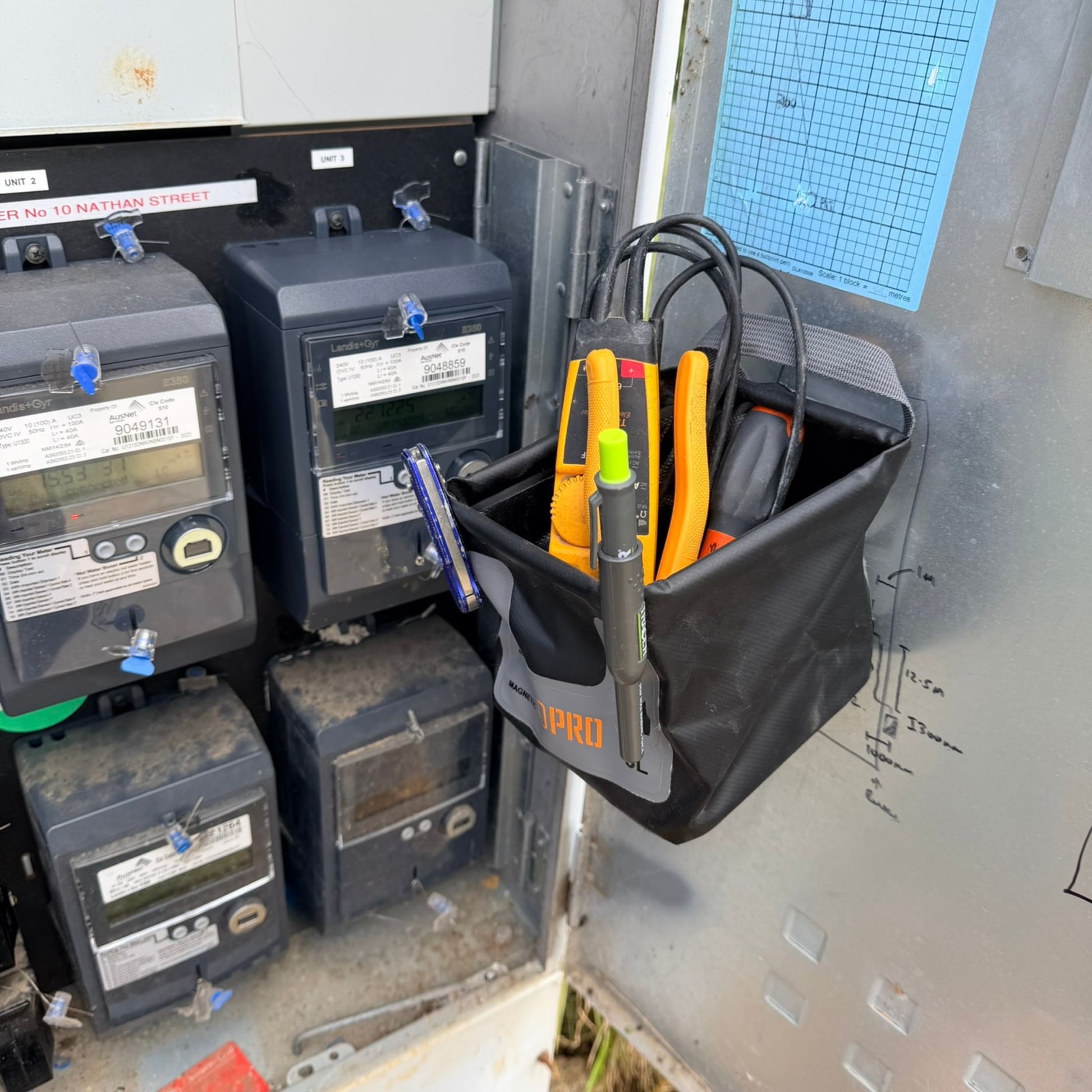 Utility box with electrical meters and a 3L Pro Magnetic Folding Bucket On Site containing tools.