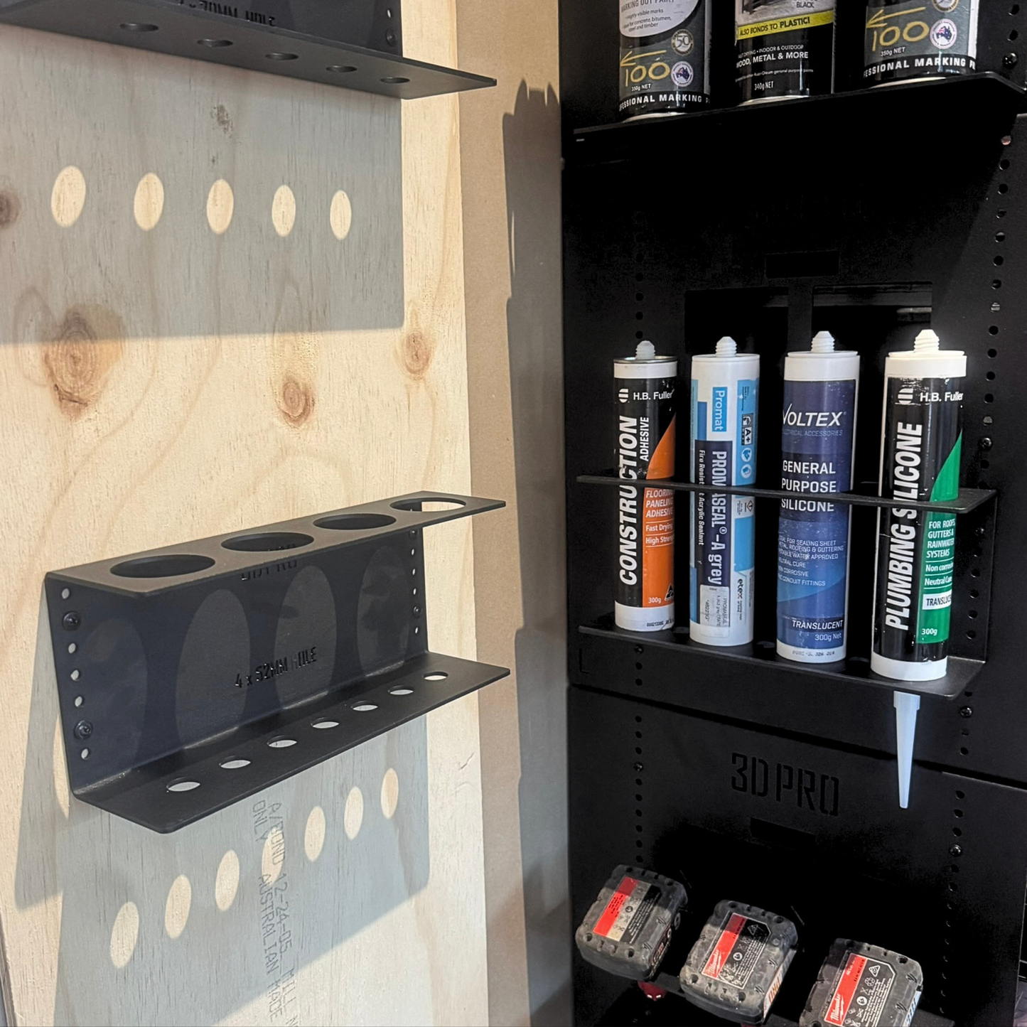Quad Silicon Holder with various cans of spray paint and tools against a wooden wall.
