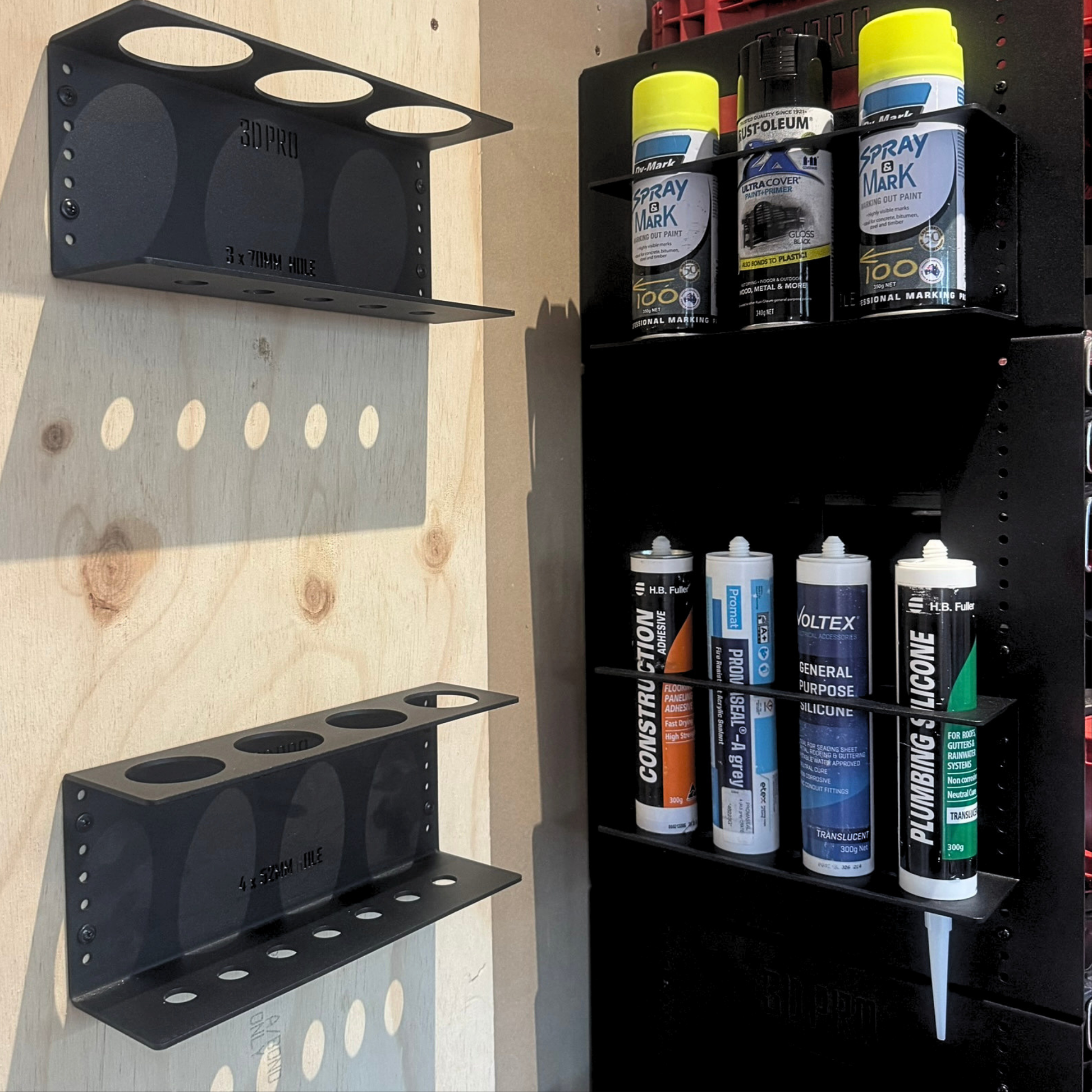 Black quad silicon holder with various cans of spray paint and chemicals against a wooden background.