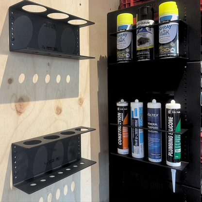 Black quad silicon holder with various cans of spray paint and chemicals against a wooden background.
