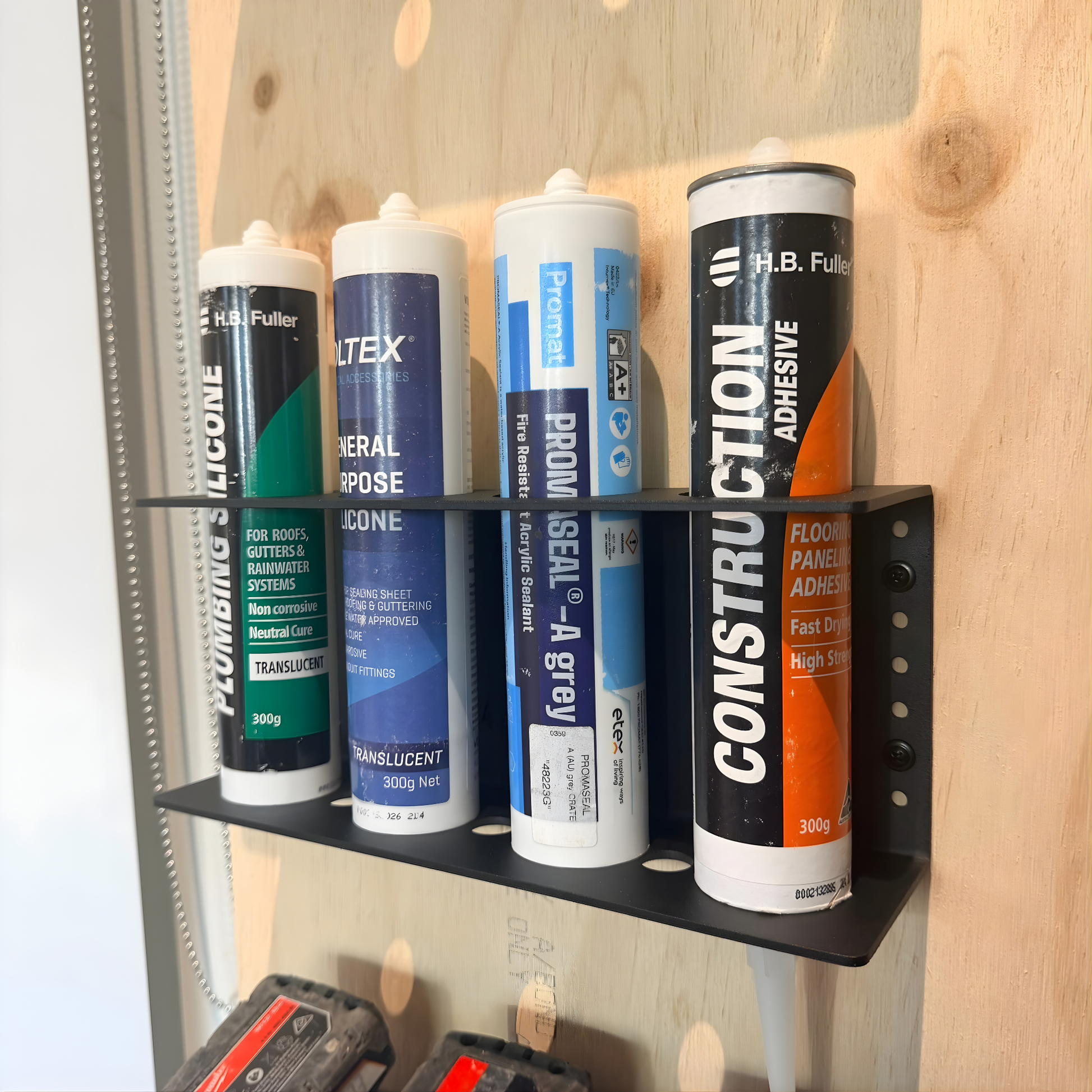 Collection of adhesive tubes on a quad silicon holder against a wooden wall.