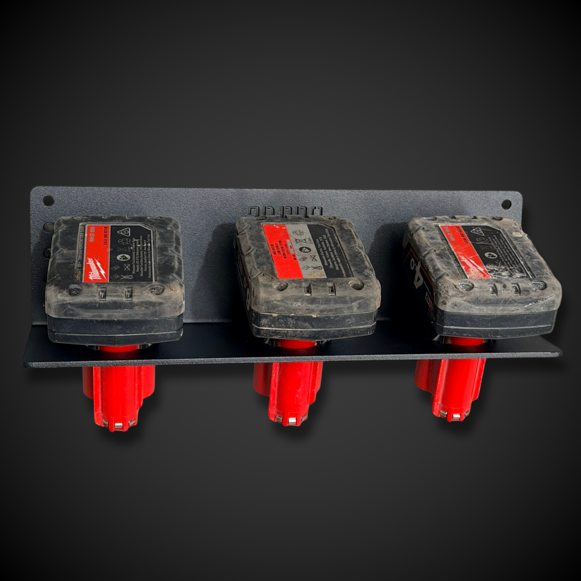Three gray and red electrical Milwaukee batteries on a black background